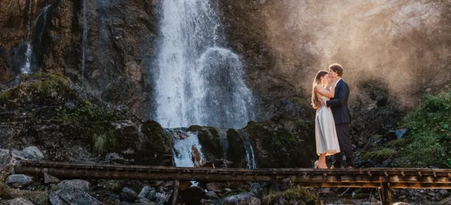 A couple beside a waterfall in golden mist in the Austrian Alps