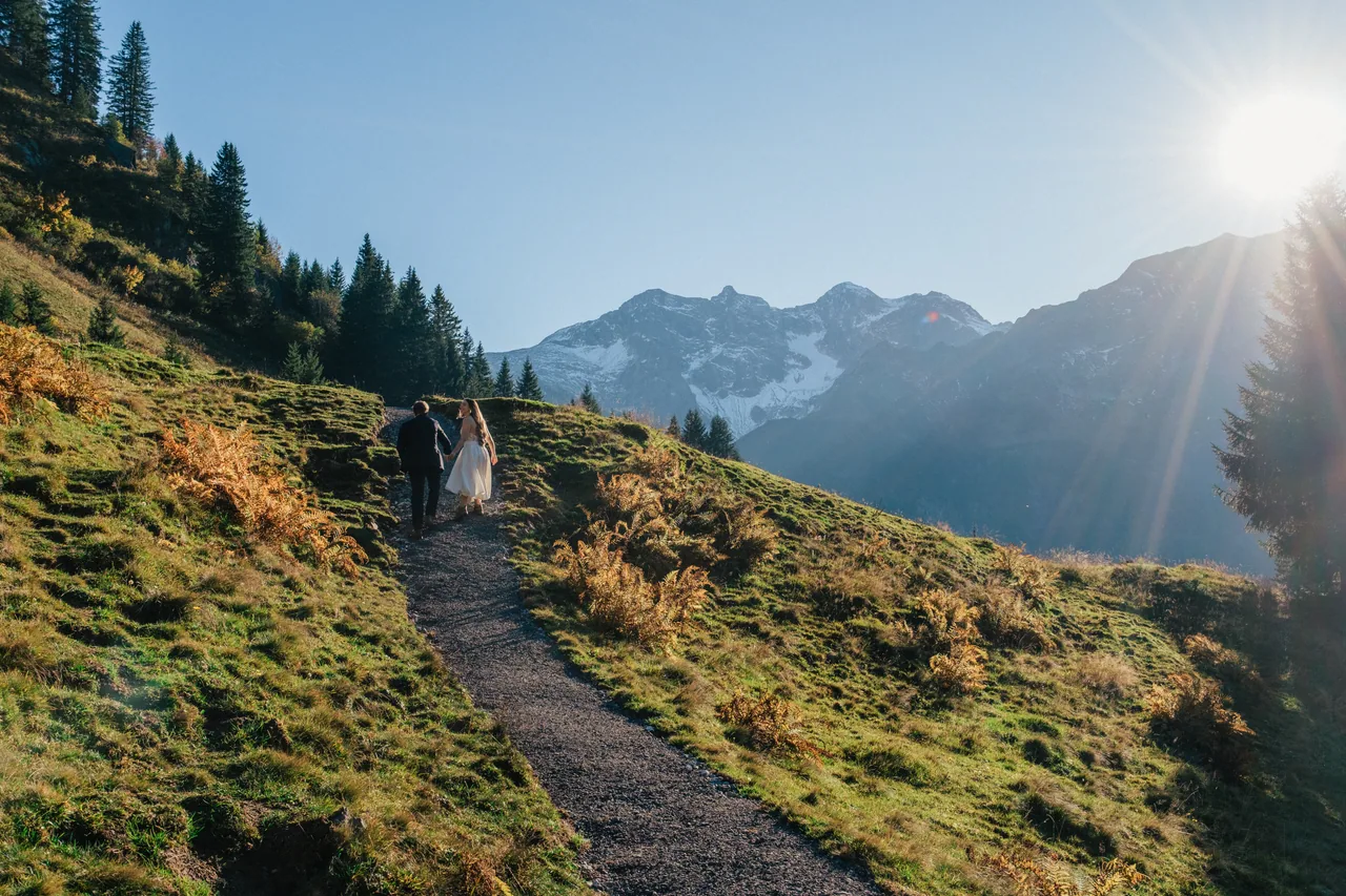 Eloping couple walking a golden mountain trail in the Austrian Alps at sunset