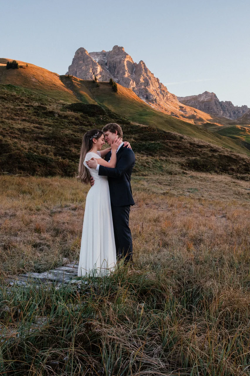 An eloping couple alone in a golden alpine meadow below a jagged peak