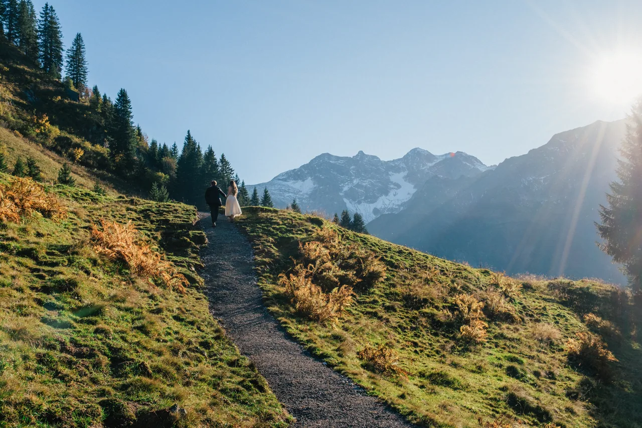 A couple on a mountain trail below alpine peaks in low sun