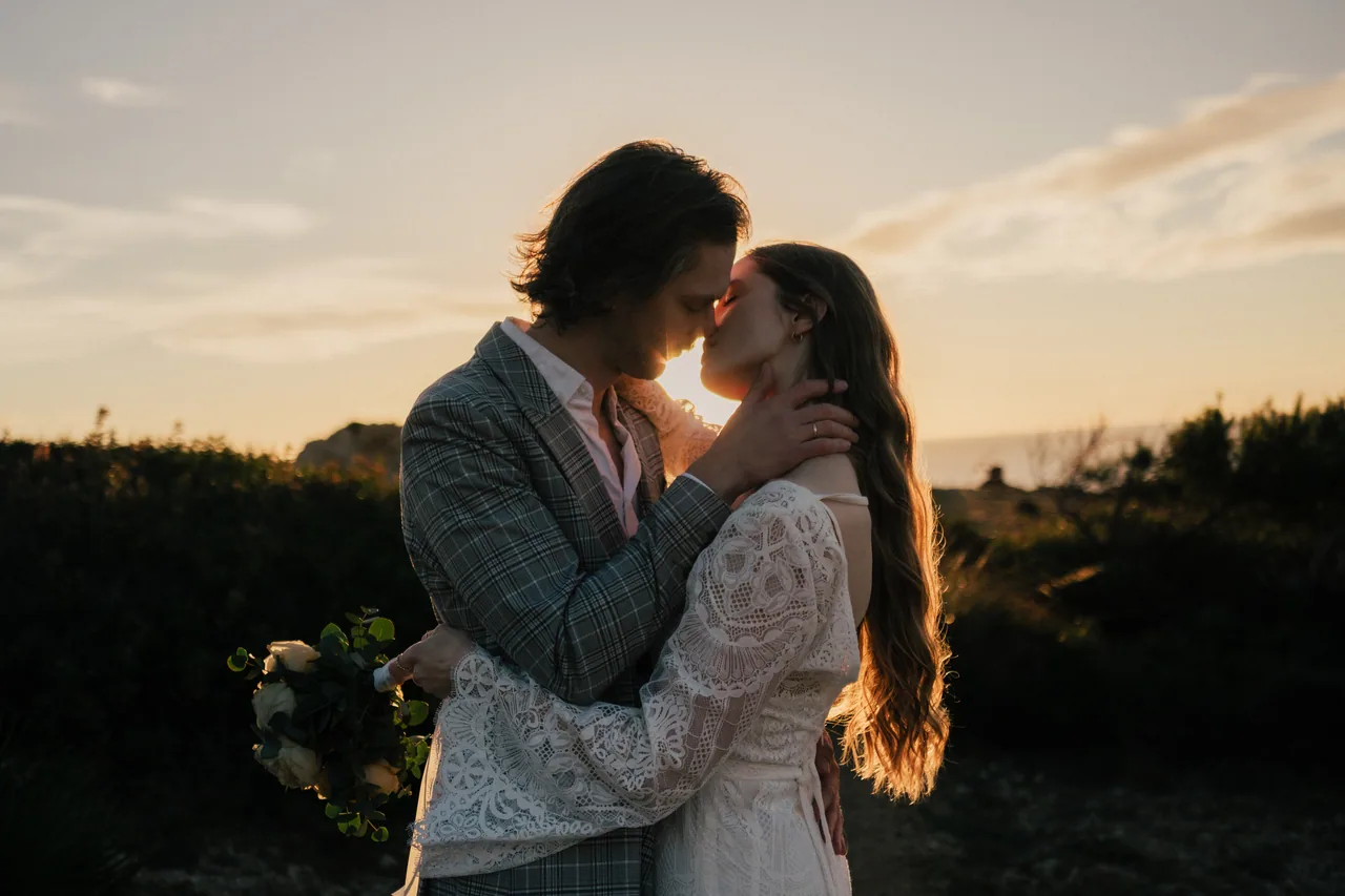 A couple embracing on a sea cliff as the sun drops into the sea on Mallorca