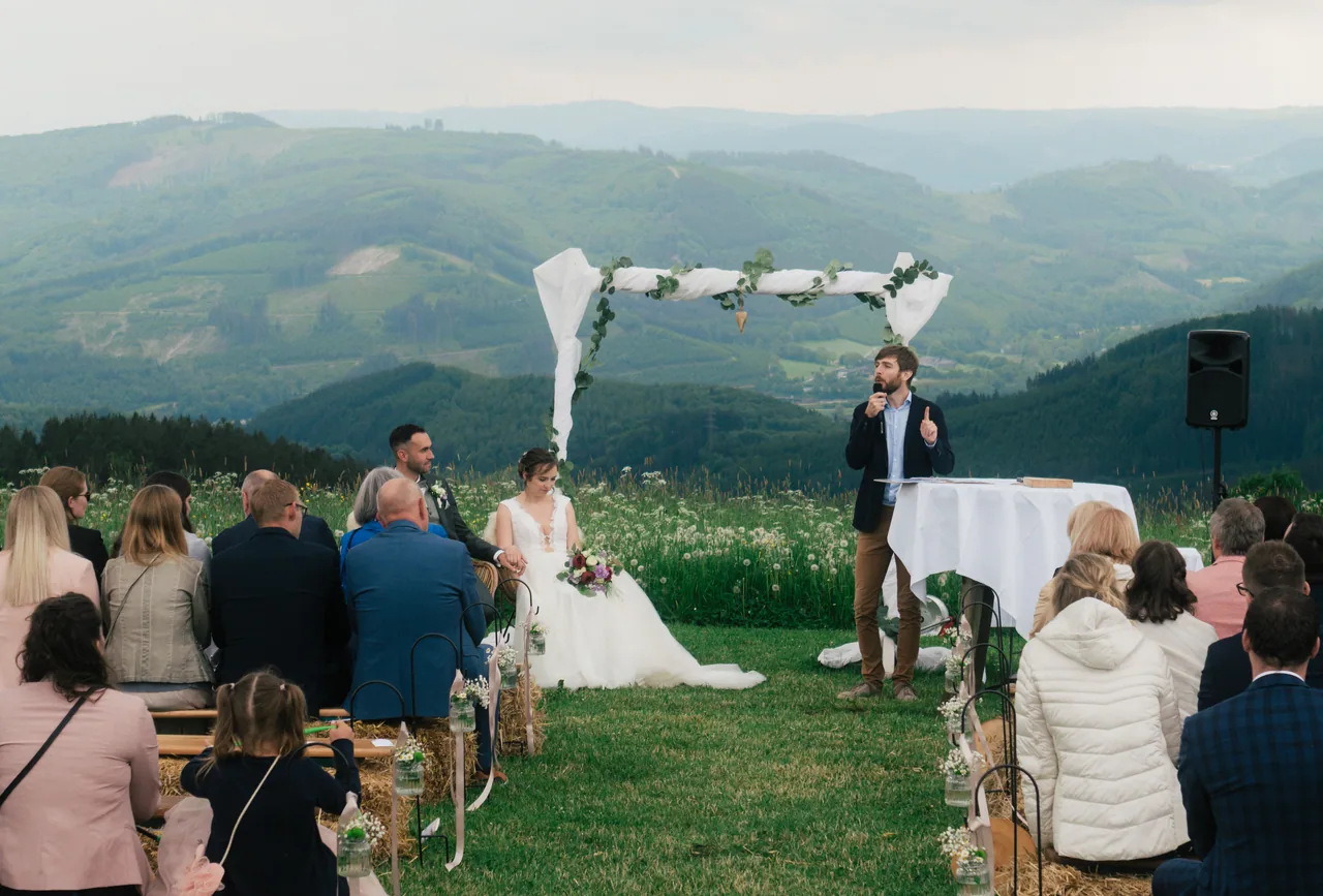 A small outdoor wedding ceremony with guests seated before a wide valley view