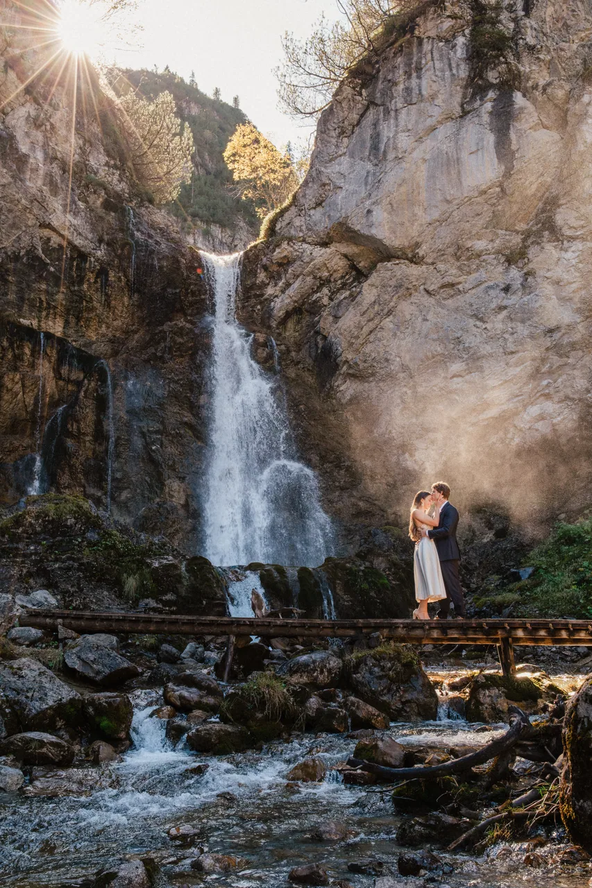 A couple beside an alpine waterfall in golden mist