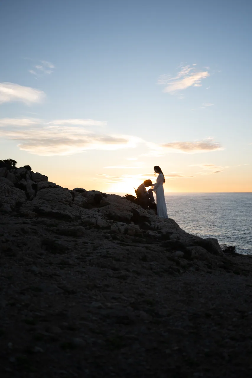 A couple at the edge of a clifftop at sunset
