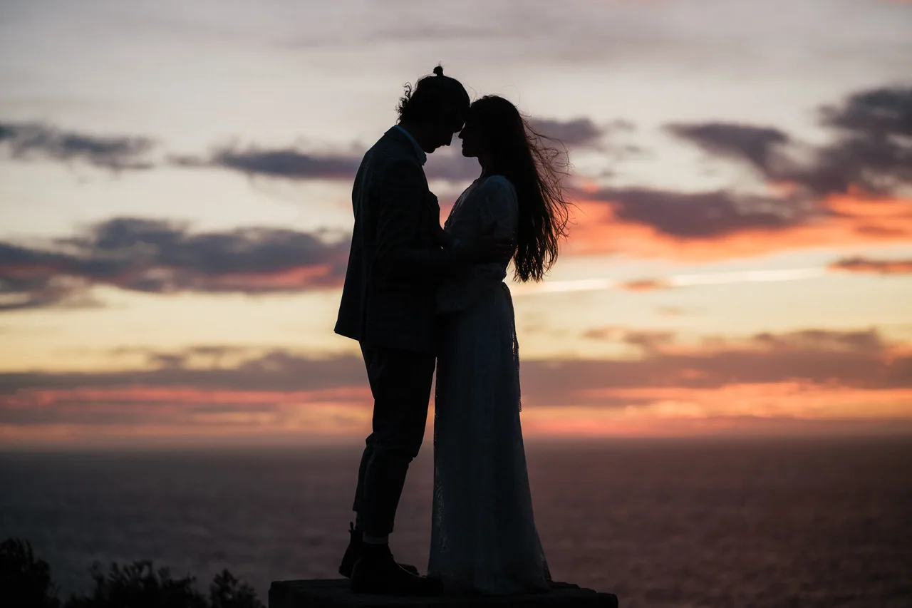 A couple silhouetted on a sea cliff at sunset