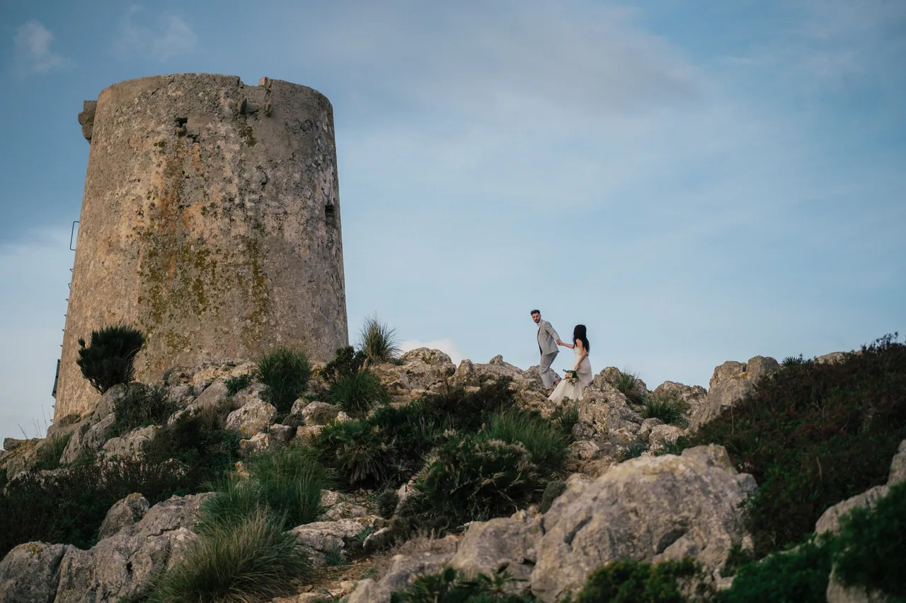 A couple walking below an old watchtower on the Mallorcan coast